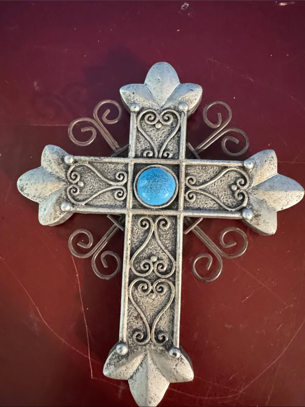 Silver-tone wall cross features a central turquoise stone and scrollwork detail